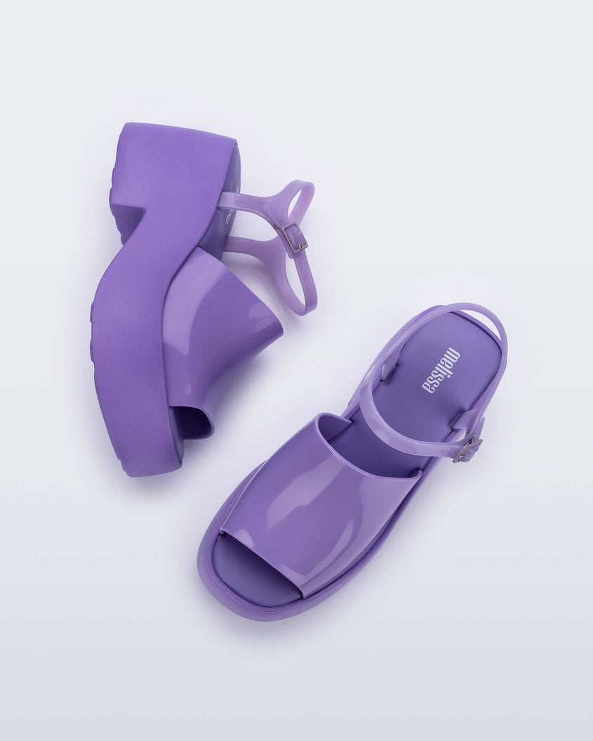 A side and top view of a pair of lilac Melissa Pose platform sandals with a lilac front strap, a clear lilac ankle strap and a lilac sole.