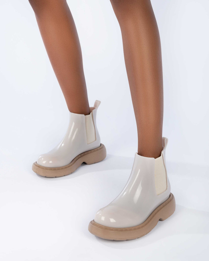 Closeup of a model's legs wearing a pair of Melissa Step slip on ankle boots with beige upper and brown lugg sole 