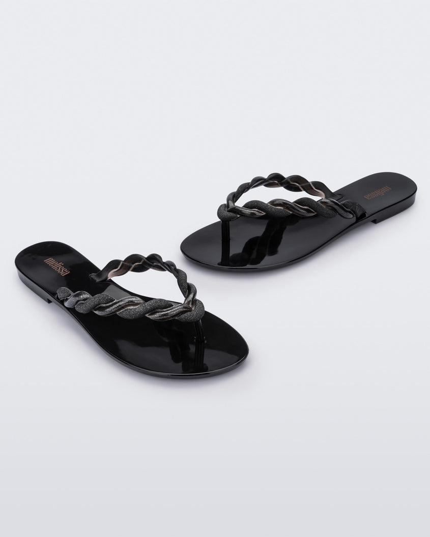 An angled front and side view of a pair of Black/Gold Melissa Louise Flip Flops with glitter twisted rope like straps.