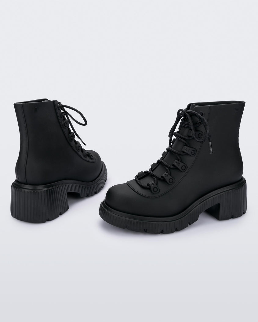 A back and side view of a pair of matte black Melissa Cosmo boots with a black base, laces and heel sole, laying on their side.