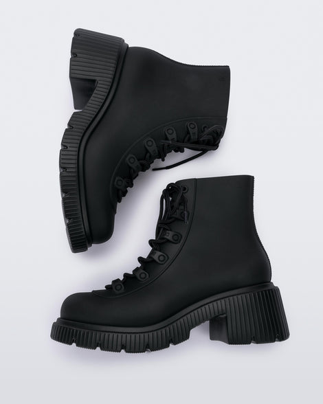 A side view of a pair of matte black Melissa Cosmo boots with a black base, laces and heel sole, laying on their side.
