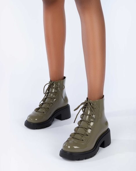 A model's legs wearing a pair of black/green Melissa Cosmo boots with a green base, laces and a black heel sole.