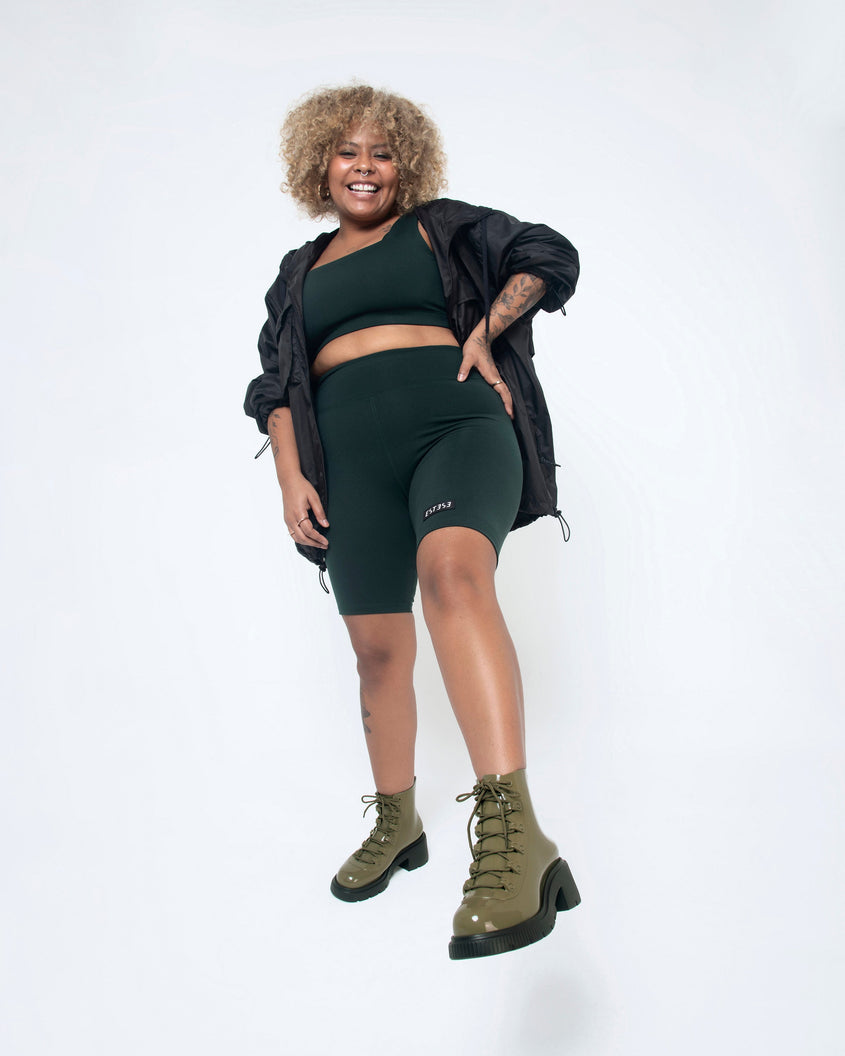 A model wearing black shorts and top is posing in a pair of black/green Melissa Cosmo boots with a green base, laces and a black heel sole.