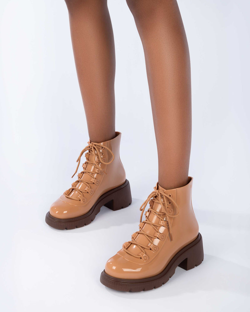 A model's legs wearing a pair of bronze/beige Melissa Cosmo boots with a bronze/beige base, laces and a brown heel sole.