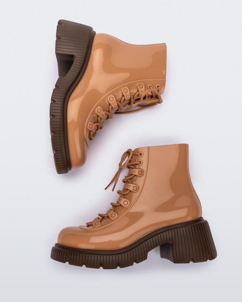 A side view of a pair of bronze/beige Melissa Cosmo boots with a bronze/beige base, laces and a brown heel sole, laying on their side.