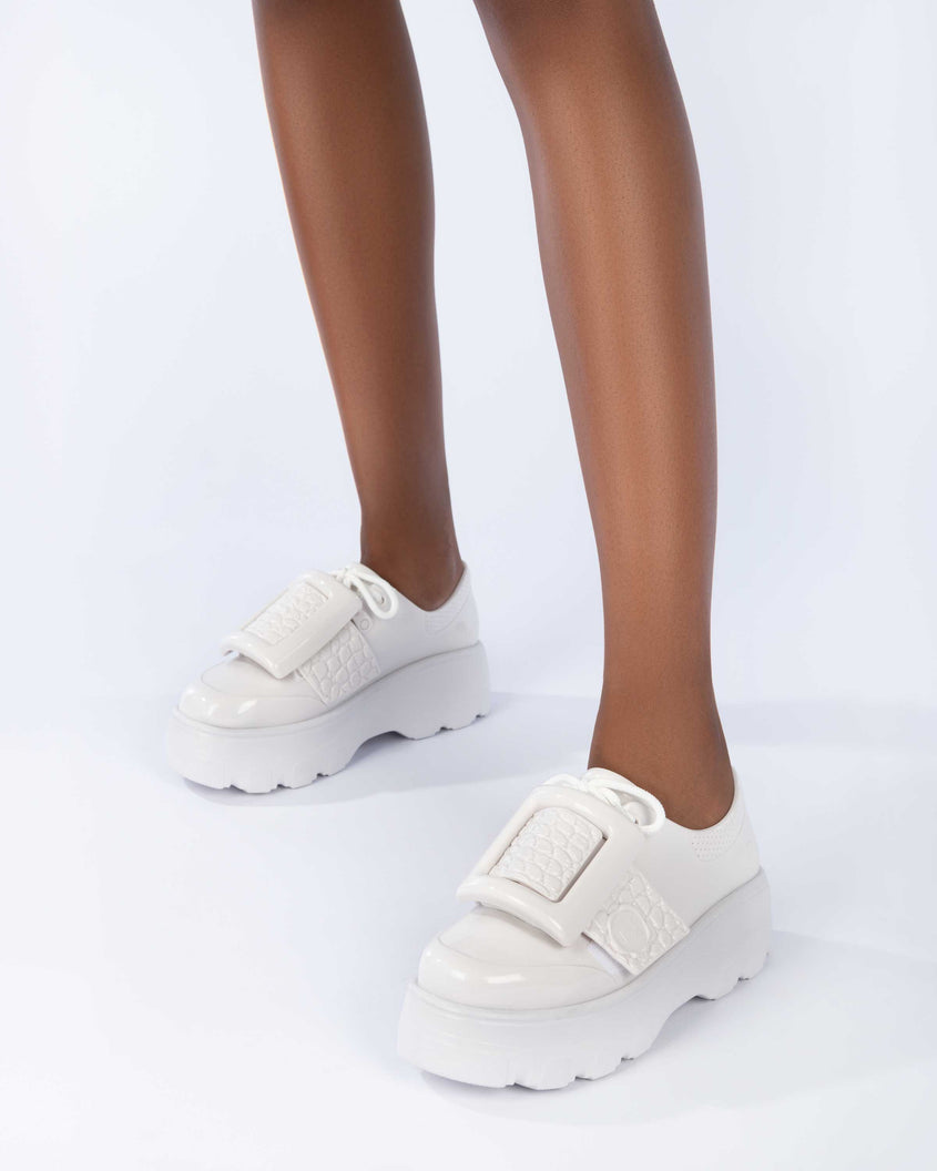 A model's legs wearing a pair of white Melissa Buckle Up Kick Off platform sneakers.