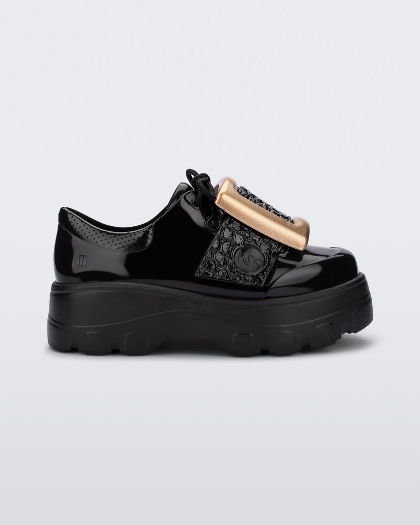 Side view of a black Melissa Buckle Up Kick Off platform sneaker with a gold buckle.