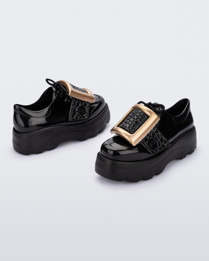 Angled view of a pair of black Melissa Buckle Up Kick Off platform sneakers with a gold buckle.