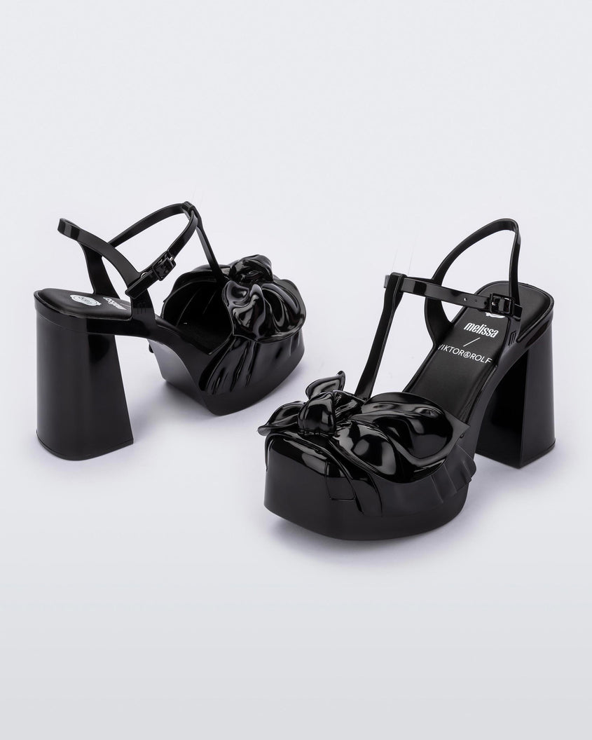 An angled side view of a pair of black Melissa Tie Party Heels with several straps and a bow on the toe.