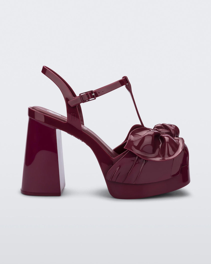 Side view of a red Melissa Tie Party Heel with several straps and a bow on the toe.