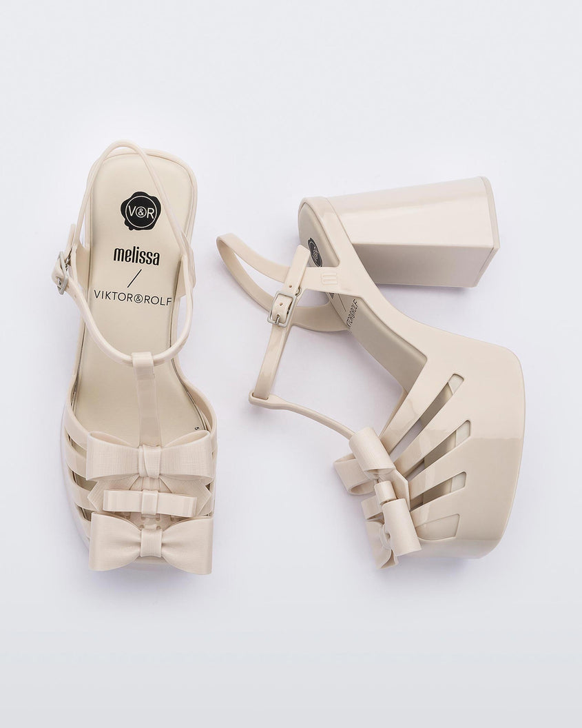 Top and side view of a pair of Melissa Tie Party platform heel sandals in Beige with ankle strap and buckle closure and 3D bow detail on front straps
