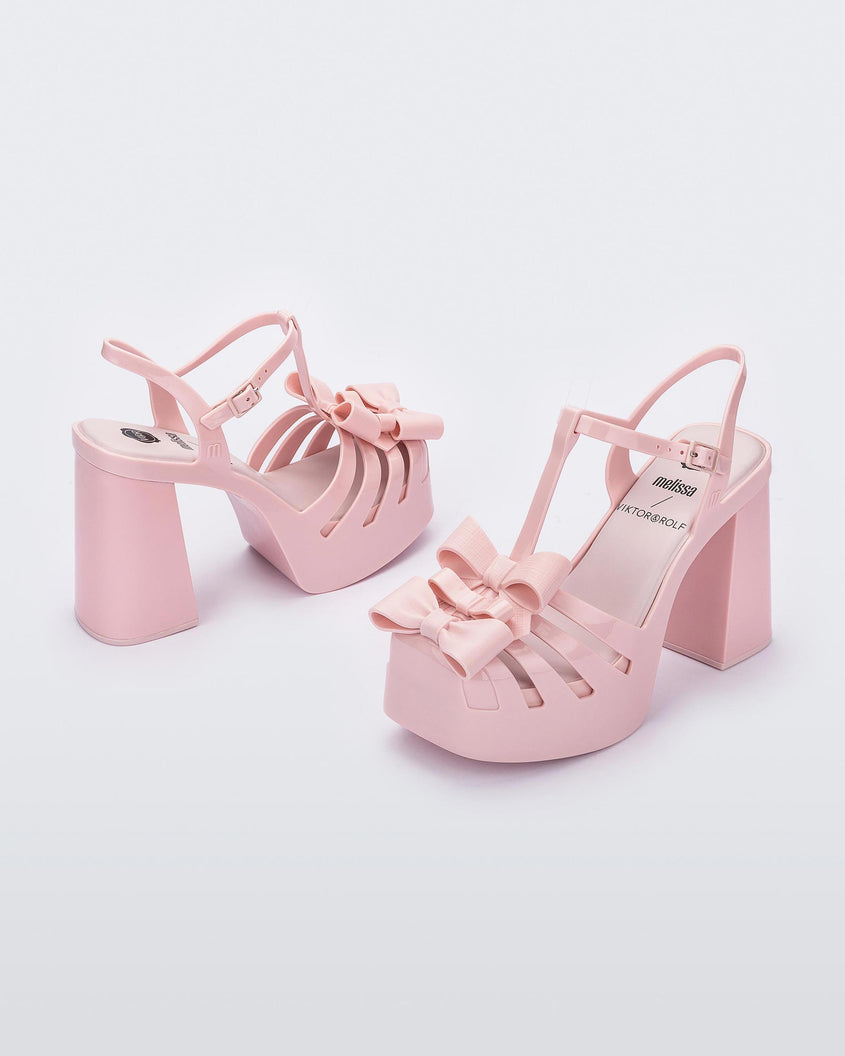 Angled view of a pair of Melissa Tie Party platform heels in Pink with 3D bow detail and ankle strap with buckle. 