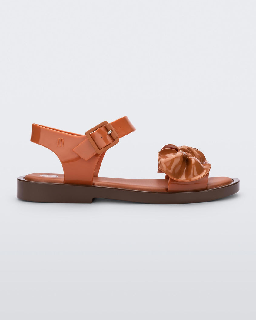 Side view of a Brown/Orange Melissa Tie Mar Sandal with an orange/brown base, an ankle strap and a front strap with a beige bow on the front.