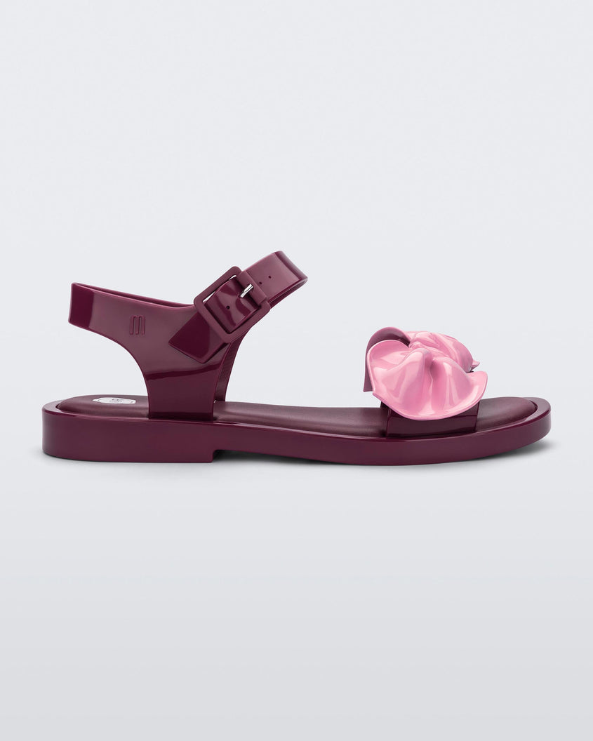 Side view of a red/pink Melissa Tie Mar Sandal with a red base, an ankle strap and a front strap with a pink bow on the front.