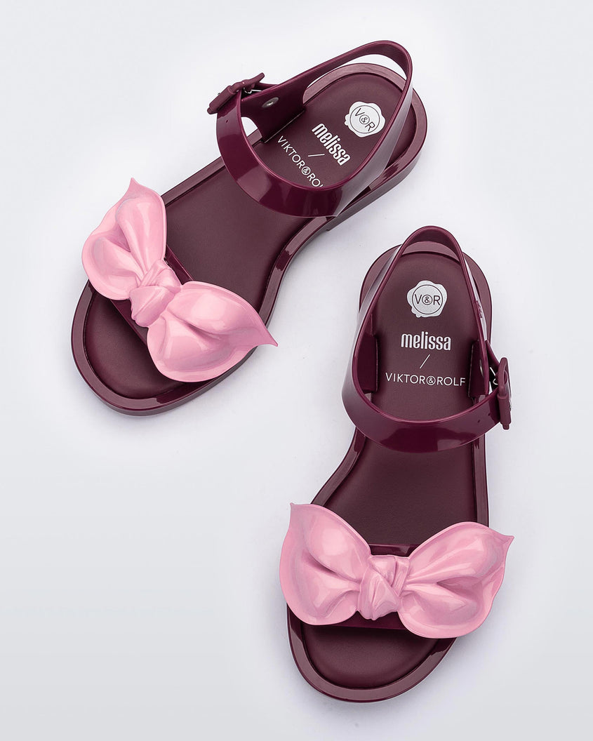 A top view of a pair of red/pink Melissa Tie Mar Sandals with a red base, an ankle strap and a front strap with a pink bow on the front.