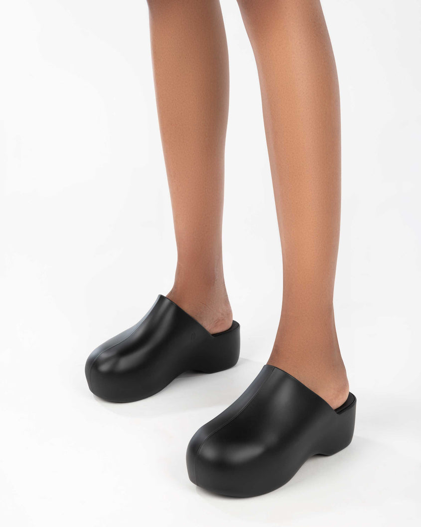 A model's legs wearing a pair of black Melissa Bubble clogs from the Simon Miller collaboration.