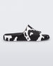 Side view of a pair of black and white cow print Melissa Cloud slides with a black insole reading in blue 