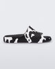 Side view of a pair of black and white cow print Melissa Cloud slides with a black insole reading in blue 