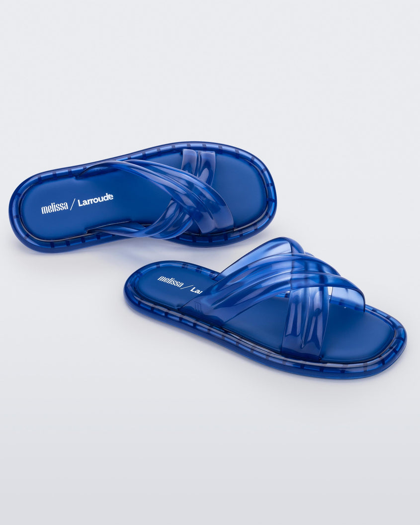 Top and side view of a pair of transparent blue Melissa Cali slides with cross straps.