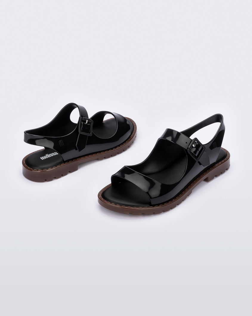 Angled view of a pair of black Melissa Bae sandals with brown soles. 