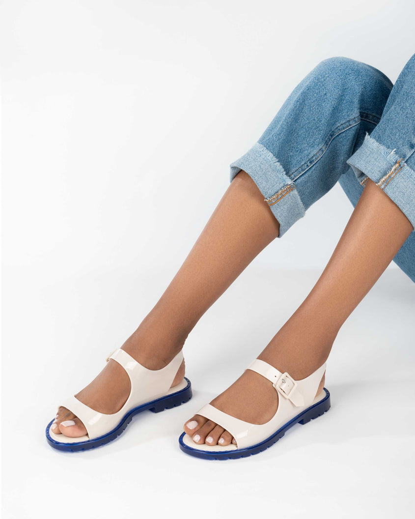 A model's legs wearing a pair of white Melissa Bae sandals with blue soles.