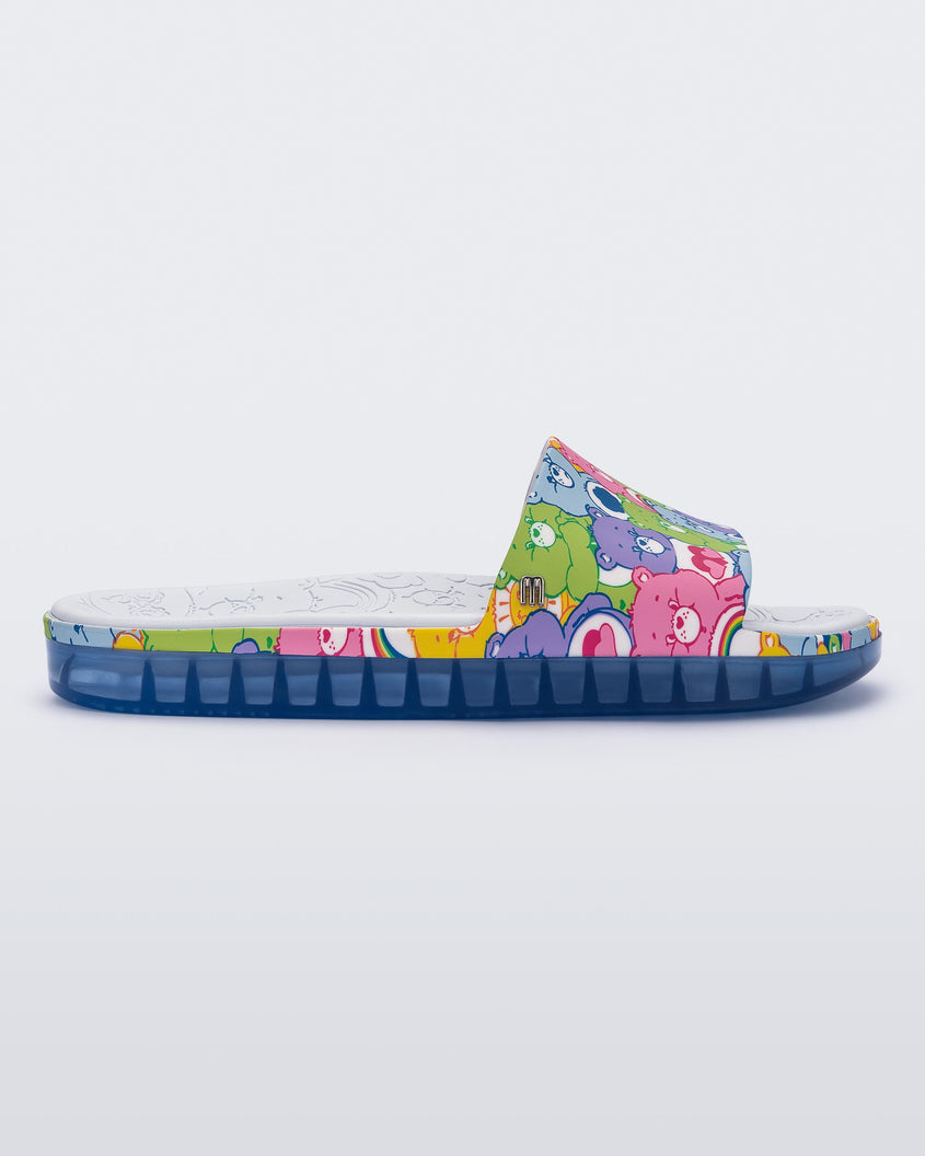 Side view of a blue Melissa Beach slide with a pattern of lilac, green, pink and blue colored care bears on the top strap, and a care bear patterend gray insole.