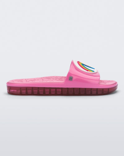 Side view of a pink Melissa Beach slide with a rainbow on a white circle on the top strap, and a care bear patterend pink insole.