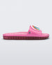 Side view of a pink Melissa Beach slide with a rainbow on a white circle on the top strap, and a care bear patterend pink insole.
