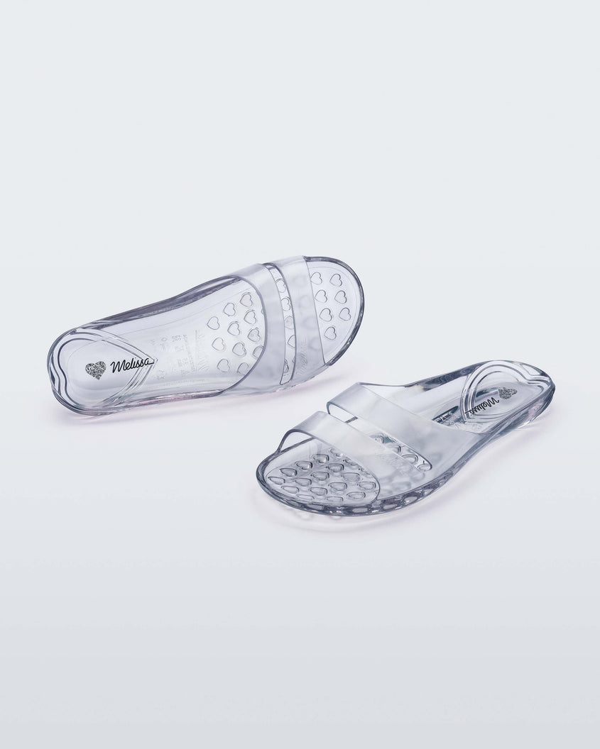 An angled front and top view of a pair of clear Melissa Real Jelly Slides with two front straps.