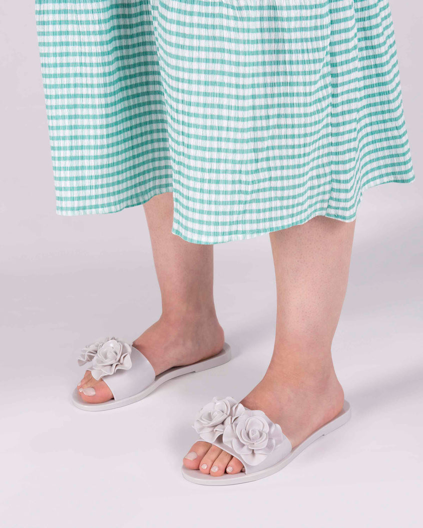 A model's legs wearing green gingham printed dress and a pair of white Melissa Babe Garden slides with two flowers on the front strap.
