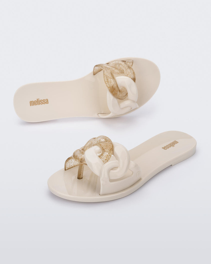 An angled top and side view of a pair of beige Melissa Jelly Chain slides with a beige and clear gold glitter chain detail.