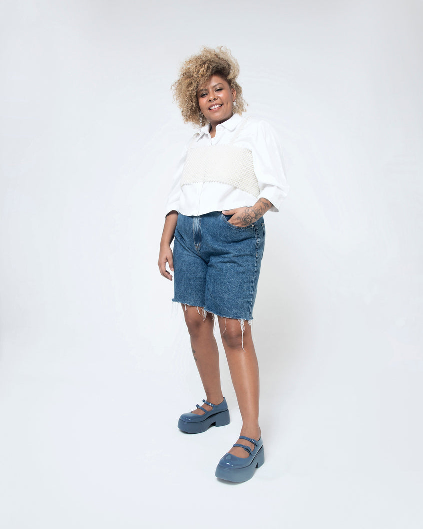 A model posing for a picture wearing a pair of blue Melissa Farah platform shoes with two straps fastened by blue buckles.