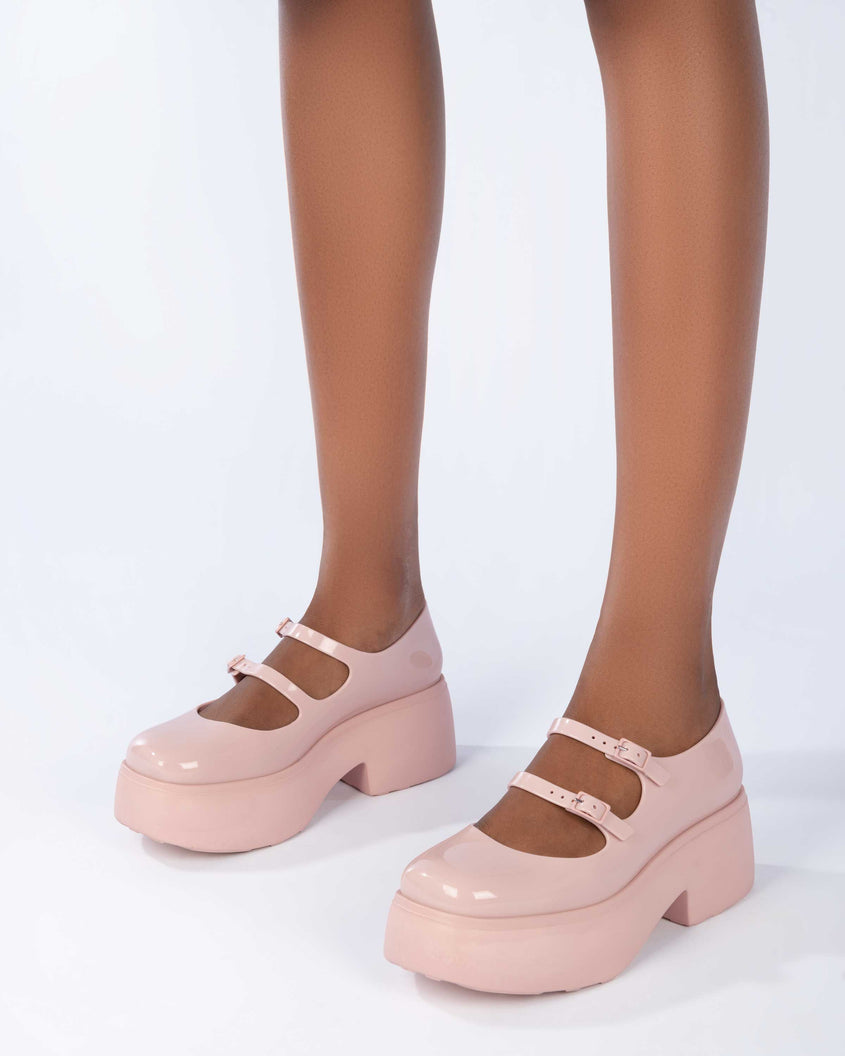 A model's legs wearing a pair of pink Melissa Farah platform shoes with two straps fastened by pink buckles.