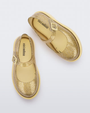 Top view of a pair of glitter yellow Mini Melissa Lola loafers with a rounded toe, strap and yellow buckle.