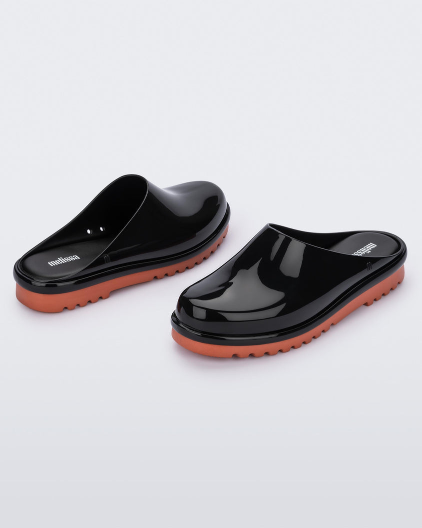 An angled front and back view of a pair of black Melissa Smart Clogs with a black base and an orange/brown sole.