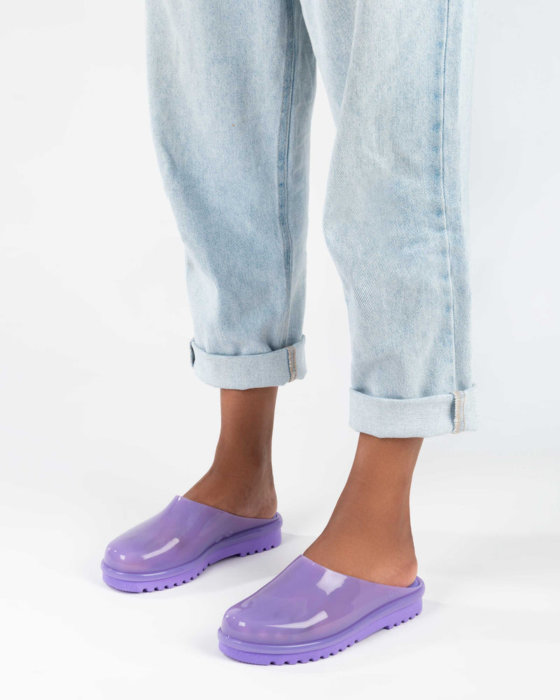 A model's legs in denim, wearing a pair of lilac Melissa Smart Clogs.