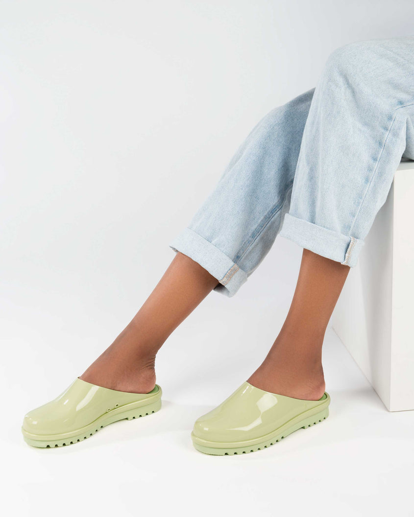 A model's legs wearing denim and a pair of green Melissa Smart Clogs.