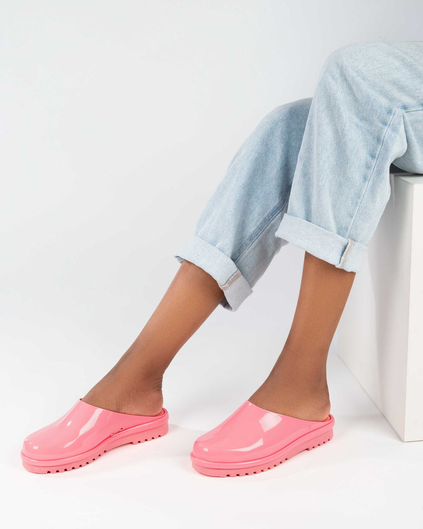 A model's legs in denim and a pair of pink Melissa Smart Clogs.