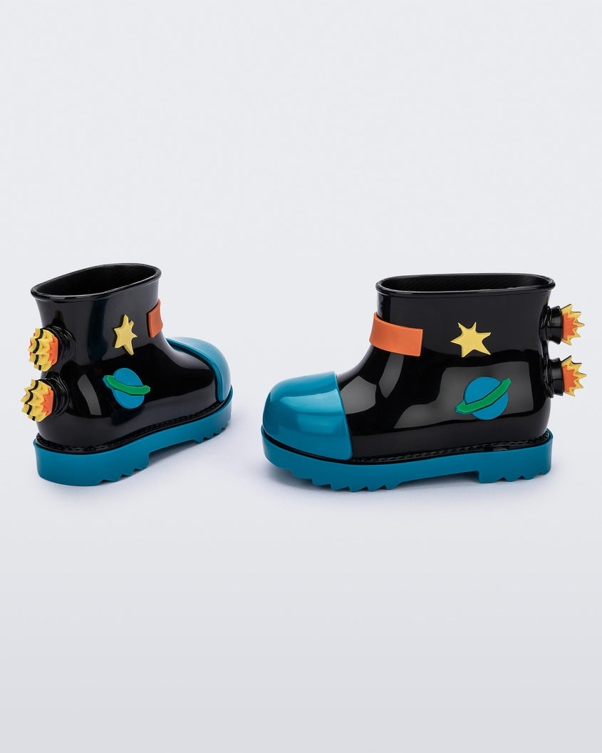 An angled side and back view of a pair of blue/black Mini Melissa Rain Boots with a black base, blue toe, blue sole, and a planet, star and fire detail on the side and back.