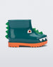 Side view of a orange/green Mini Melissa Rain Boot with a green base, orange sole, light green triangle details, white triangle details in the front and a set of orange eyes which looks like a dinosaurs face,