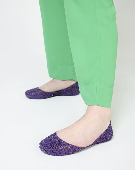 A person wearing a pair of Melissa Campana flats in purple with light green pants