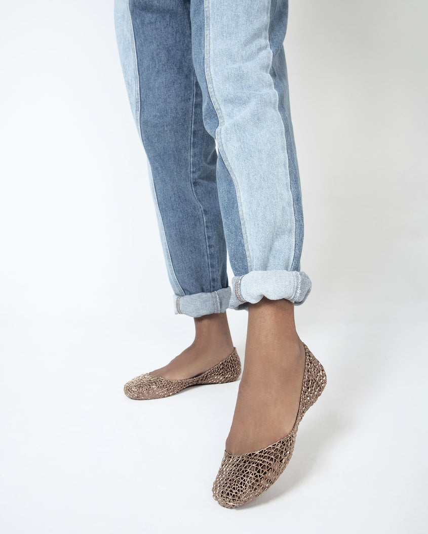 A close up of a model's legs with a pair of metallic gold Melissa Campana flats worn with cuffed jeans. 