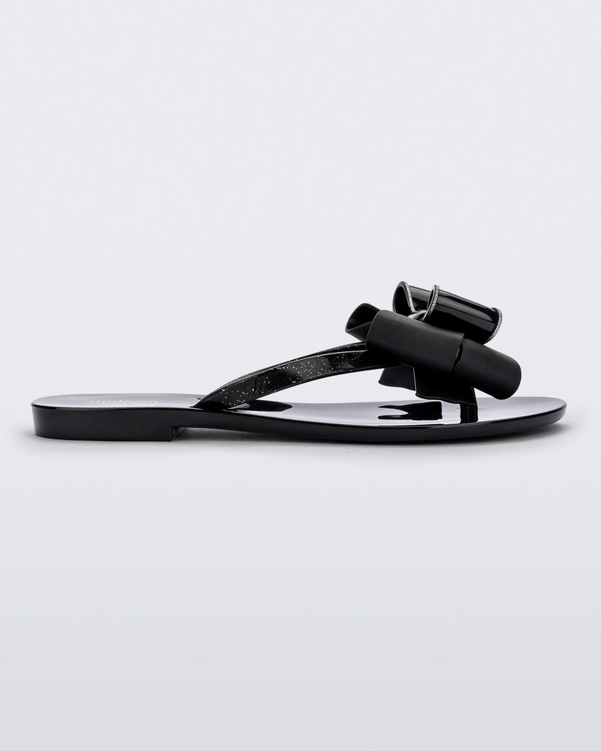 Side view of a black Melissa Harmonic Sweet flip flop with a black and glitter bow.