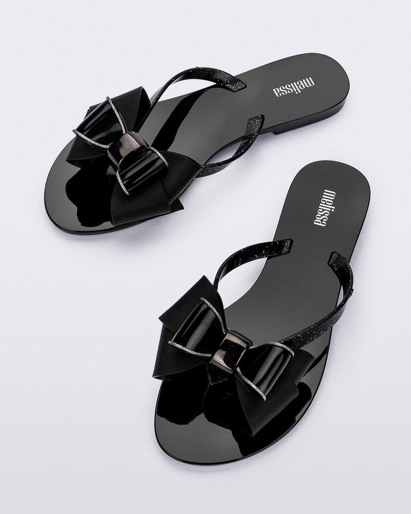 Top view of a pair of black Melissa Harmonic Sweet flip flops with a black and glitter bow.