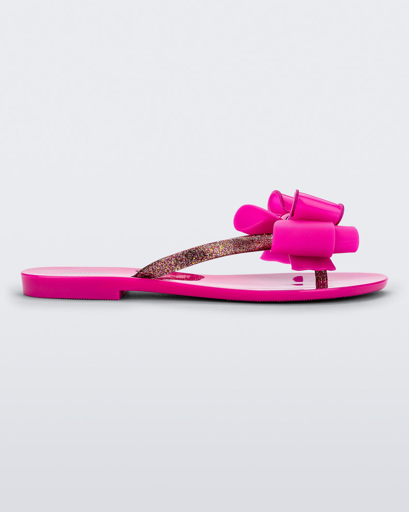 Side view of a dark pink Melissa Harmonic Sweet flip flop with a pink bow and multicolor glitter straps.