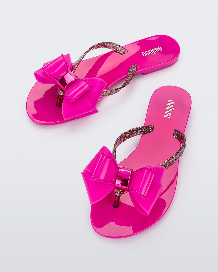 Top view of a pair of dark pink Melissa Harmonic Sweet flip flops with a pink bow and multicolor glitter straps.