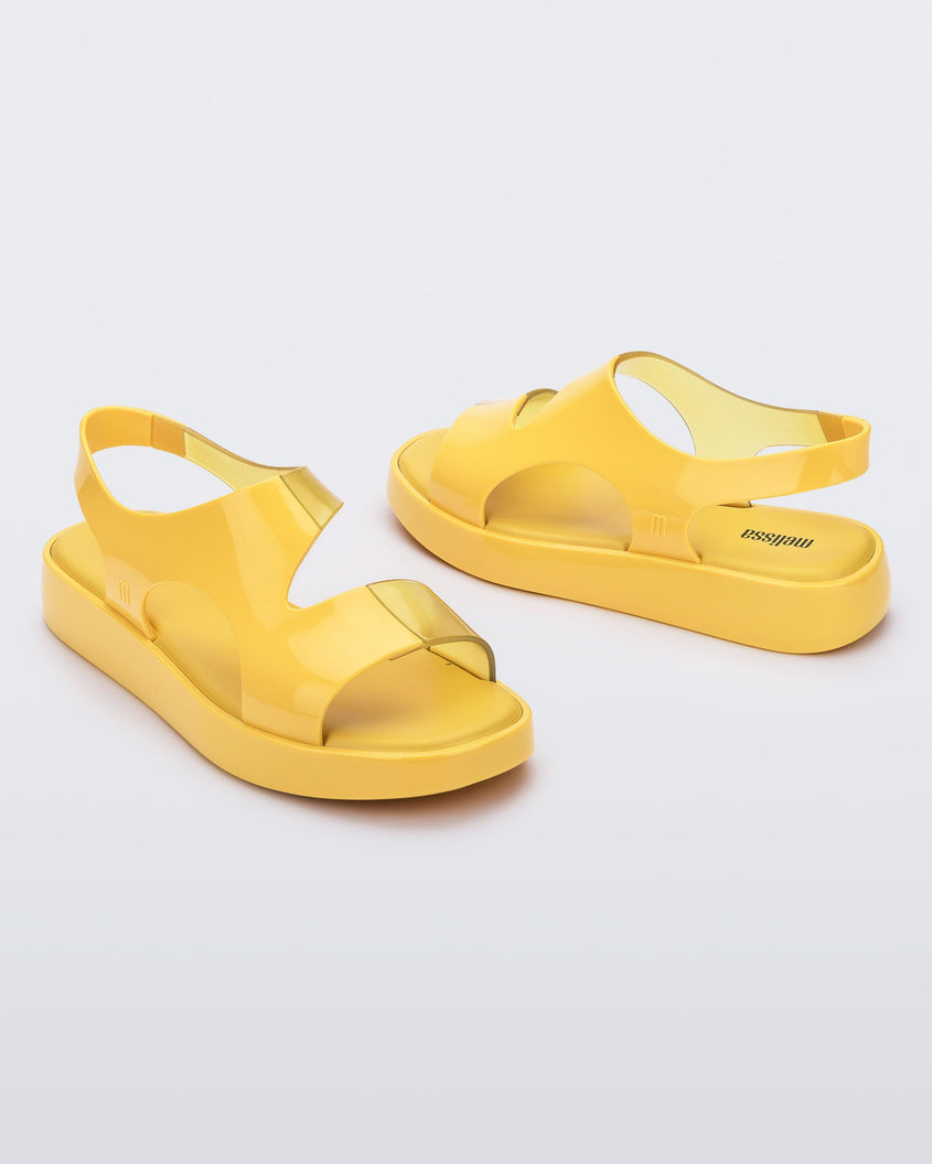 A side and angled view of a pair of yellow Melissa Franny sandals with straps.