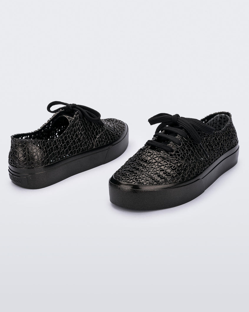 An angled front and back view of a pair of black Melissa Campana sneakers with a woven texture base and laces.