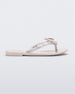Side view of a beige / metallic white Mini Melissa's Harmonic Bugs flip flop with a clear glitter bug with a silver buckle on the straps.