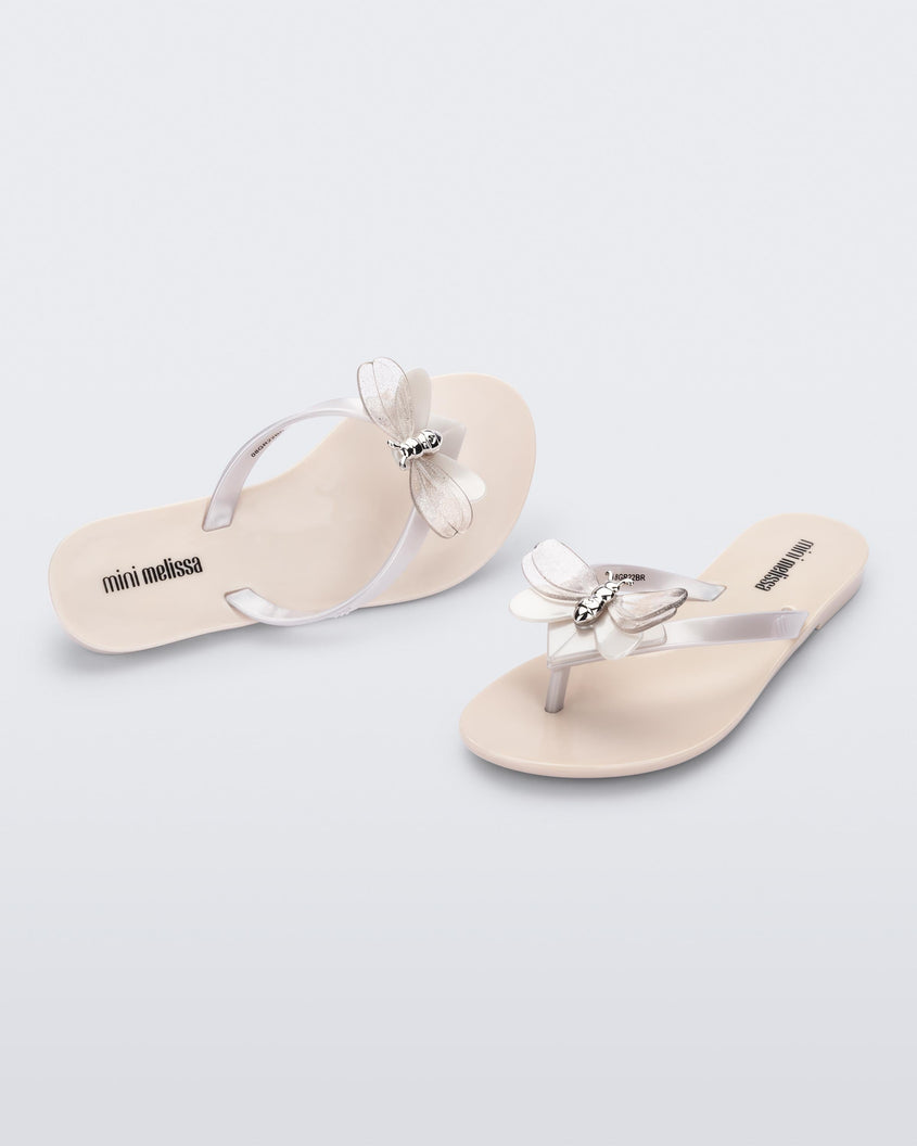 An angled and front view of a pair of beige / metallic white Mini Melissa's Harmonic Bugs flip flop with a clear glitter bug with a silver buckle on the straps.